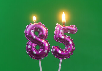 Burning air balloon shaped pink birthday candles with hearts on green background, number 85	