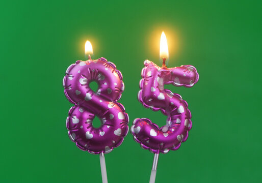 Burning air balloon shaped pink birthday candles with hearts on green background, number 85	