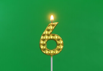 Burning gold birthday candle on green background, number 6