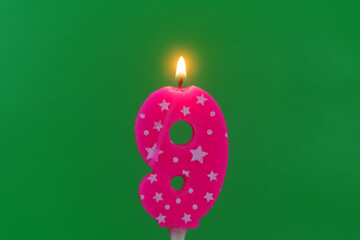 Burning pink with white stars birthday cake candle on green background. Number 9