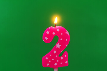 Burning pink with white stars birthday cake candle on green background. Number 2