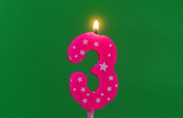Burning pink with white stars birthday cake candle on green background. Number 3
