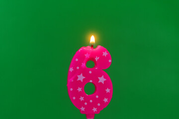 Burning pink with white stars birthday cake candle on green background. Number 6
