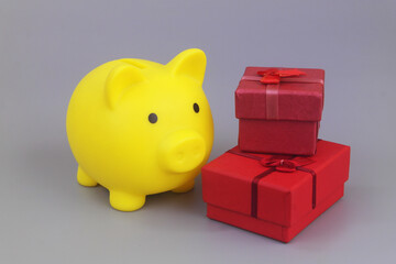 Yellow piggy bank with two gift boxes on grey. Saving money for gifts concept.