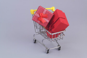 Gift boxes in shopping cart on grey background.