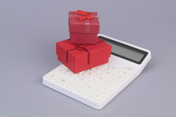 Red gift boxes on calculator on grey background. Gifts price concept.