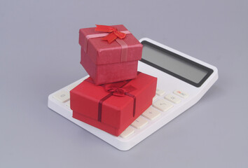 Red gift boxes on calculator on grey background. Gifts price concept.