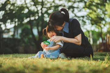 Happy Asian mother and toddler daughter exploring nature with a magnifying glass in a green park