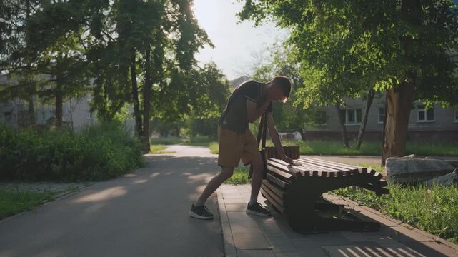 Person Attentively Inspecting Wooden Bench Gap, Male Figure Focused On Analyzing Space Between Bench Slats, Man With Careful Hands Examining Wooden Slat Gap In Peaceful Suburban Park Setting