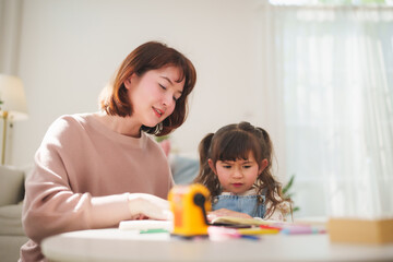 Naklejka premium Asian woman helps her little girl enjoy creative drawing time, supporting education, parenting, and family bonding indoors