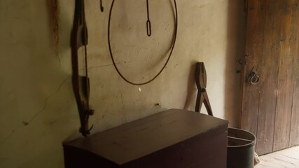 Rustic interior of historical farmhouse showing wooden chest hanging metal tools and weathered walls. Traditional dutch agricultural storage room with wooden door at open air museum exhibit.
