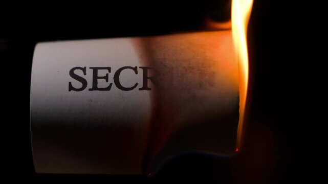 Burning sheet of paper with word SECRET, close-up on black background. Revealing secrets or hiding