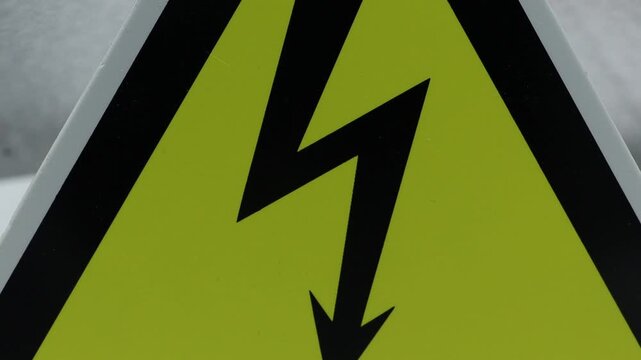 A close-up shot of a yellow electrical warning sign partially obscuring a ripe red apple. This clip highlights the unexpected contrast between danger and nature.