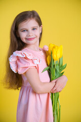 Cheerful happy girl with tulips flower bouquet in pink dress on yellow background