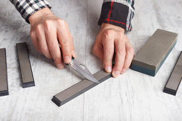 Sharpening small fishing on whetstone knife on white table.