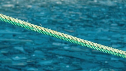 Close-up of a green marine rope stretched diagonally above cold blue water with floating broken ice. Nautical background with shallow depth of field, texture and copy space. Concept of sailing