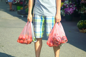 Close-up of hands carrying plastic bags with fresh produce bought at local market. Represents...