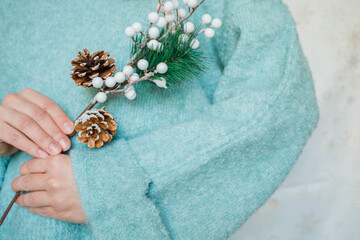 Pine Christmas conifer branch with cones in woman hands close up with copy space. Woman in warm winter mint sweater keeping festive decor branch.