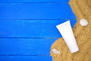 Cream tube and sand on blue wooden. Sea summer vacation background with space for the text. Top view