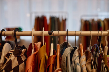Assorted second hand clothing hanging on rack in store, various garments displayed closely together, blurred background showing additional racks with pre owned clothes visible