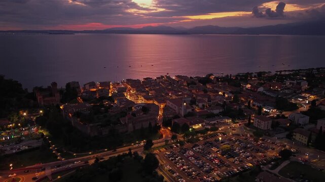 Drone footage of Lazise, Italy, overlooking Lake Garda at sunset. Bird&rsquo;s eye view of the historic town, Italian architecture, and glowing evening lights.