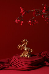 Symbol of Chinese New Year 2026. Golden horse figurine with cherry blossom on a rich red background.