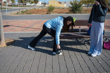 Teen girl lifting kettlebell while training outdoors with her friend during a strength workout session in a sunny urban park