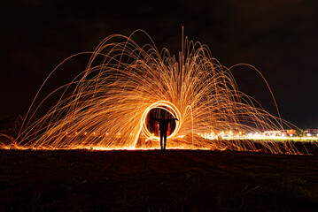 Bright sparks of a sparkler in the night sky. Firework fountain captured with long exposure, creating arc-shaped light trails in orange and golden tones. Festive atmosphere, New Year, party, magic of 