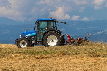 Obraz premium Tractor with attached tedder working hay on alpine slope