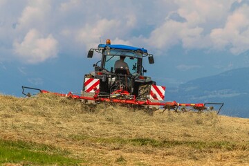 Obraz premium Tractor with attached tedder working hay on alpine slope