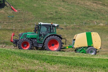 Tractor towing round baler across a grassy field