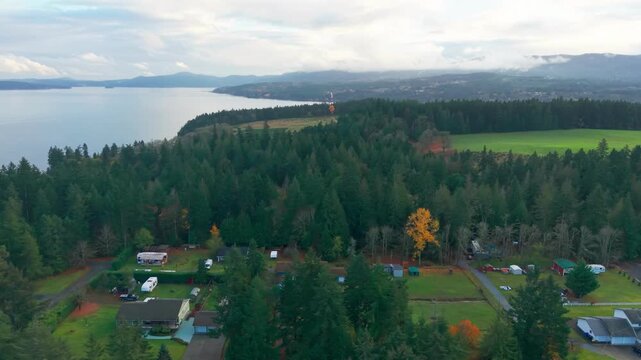 Drone footage of a rural residential neighborhood surrounded by dense evergreen forest overlooking Saanich Inlet near Mill Bay on Vancouver Island, with mountains and calm coastal waters