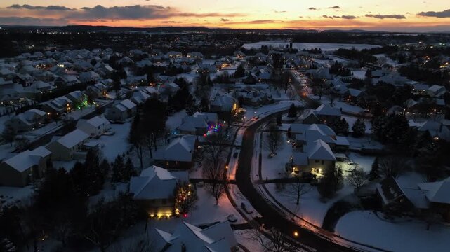 Aerial establishing shot over quiet and peaceful american neighborhood at golden sunset. Decorated houses and front yards during christmas season. Snow.covered roofs of homes. Wide shot.
