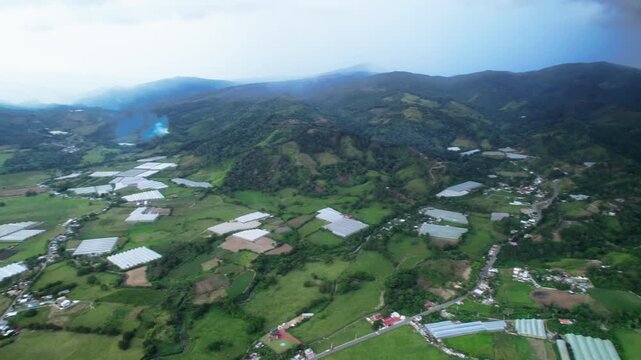Drone pan left over agricultural greenhouses in Jarabacoa valley, surrounded by mountains, vegetation and rural farming infrastructure.