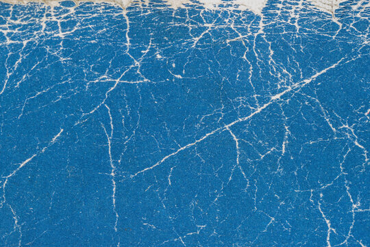 Texture of old shabby book cover close up. Blue cracked paper texture with organic white veins and worn top edge. Natural background texture