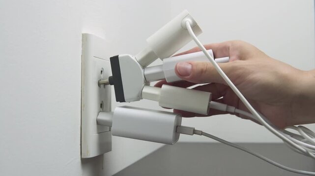 Hand inserting electrical plugs into outlet. Electrical overload