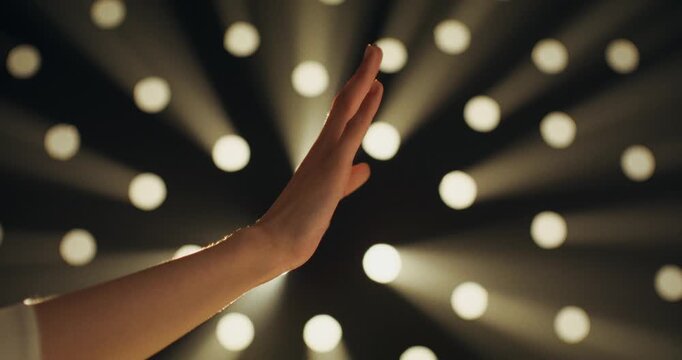 Close-up of a woman's hand on a black background in the studio. The woman moves her hand smoothly. Light breaks through the perforation in the black background