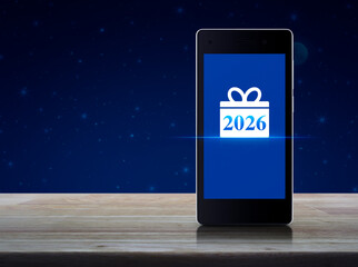 Gift box happy new year 2026 flat icon on modern smart mobile phone screen on wooden table over fantasy night sky and moon, Business happy new year 2026 shop online concept