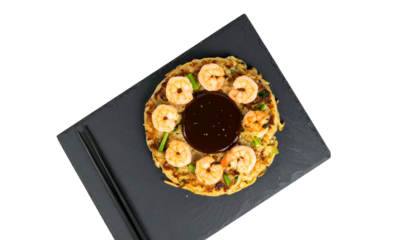 Japanese savory pancake with shrimp, sauce, and scallions on a black slate