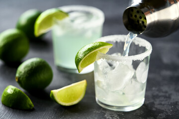 Bartender pours margarita cocktail in a glasses , selective focus on a black background.