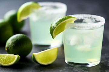 Classic lime margarita cocktail with sliced and whole limes sitting on a black table.