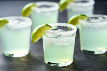 Lot of glasses filled with Margarita cocktail are lined up on a black background.