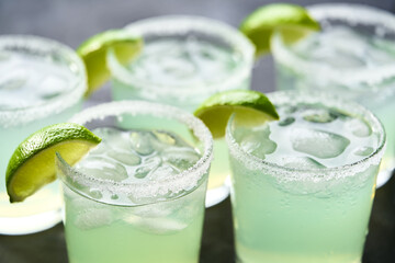 Margarita cocktail in glasses, lime and ice on black table, closeup.