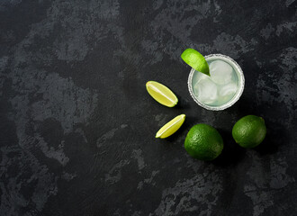 Margarita cocktail with ice cubes in glass and lime on a black table , top view.
