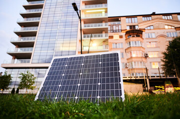 Photovoltaic solar panel in front of modern apartment building with balconies, suggesting residential or mixed-use. Concept of integration of sustainable renewable energy sources into architecture.