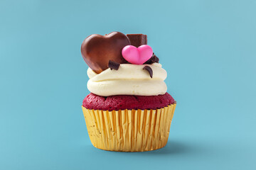 Red cupcake with cream cheese frosting and heart chocolate decorated for valentines day on blue background