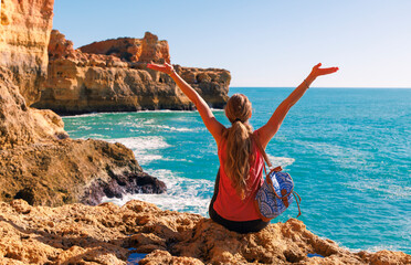 Woman sitting on rock cliff enjoying amazing view of atlantic ocean. Cave, rock formation on coast of Algarve in Portugal