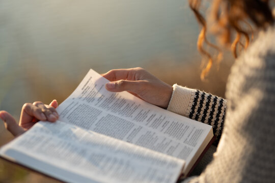 The image depicts a woman reading the Bible outdoors in soft sunlight. The concept encompasses reading the Bible and seeking God's words in the sacred texts, spiritual growth, and daily devotion.