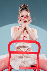 A stylish Asian fashion model poses in a studio wearing a chic coquette outfit with a cream lace corset, ruffled mini skirt, vibrant red tights, and cherry earrings for a trendy look.