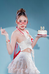 Elegant Asian beauty celebrates 30th birthday in white lace halter crop top and ruffled mini skirt with red ribbons, holding red velvet cake, wearing red heart glasses and cherry earrings, glamorous 